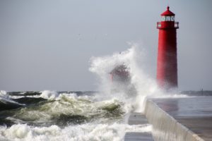 waves crushing the red lighthouse under gray sky during daytime