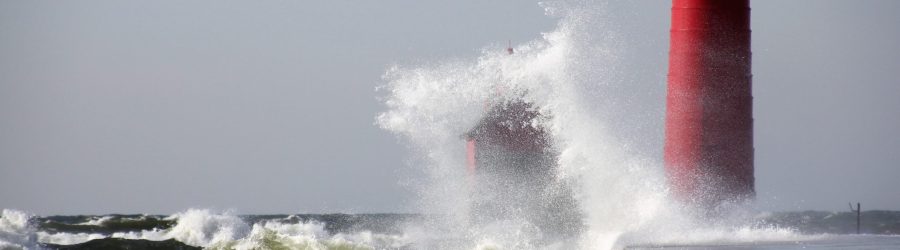 waves crushing the red lighthouse under gray sky during daytime