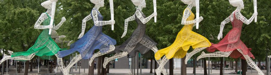 five running women wearing different dresses holding torch statue